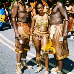 Three people in golden festival costumes outdoors.