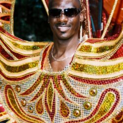 Man wearing colorful carnival costume and sunglasses.