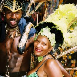Carnival performers in vibrant, feathered costumes smiling.