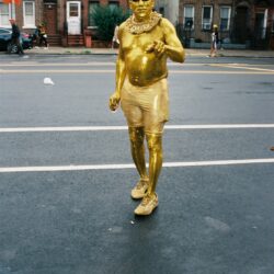 Man painted gold walking on city street.