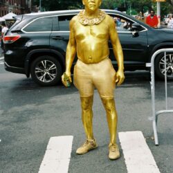 Man painted gold standing on crosswalk.