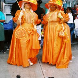 Two women in orange dresses, umbrellas.
