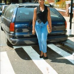 Person holding book standing by parked car